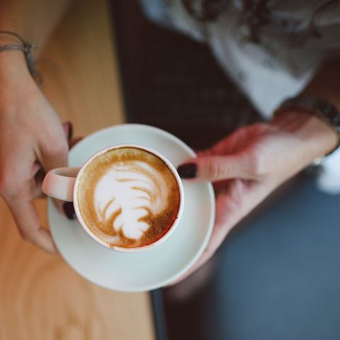 Hands holding a cappuccino with latte art at a café table (mood photo)