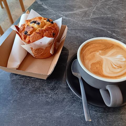 A blueberry muffin next to a latte with foam art (mood photo)